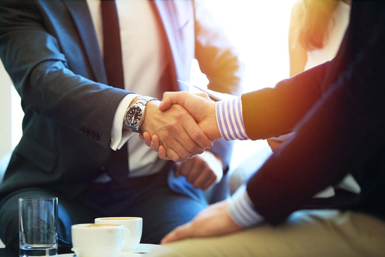 Two people shaking hands over a table.